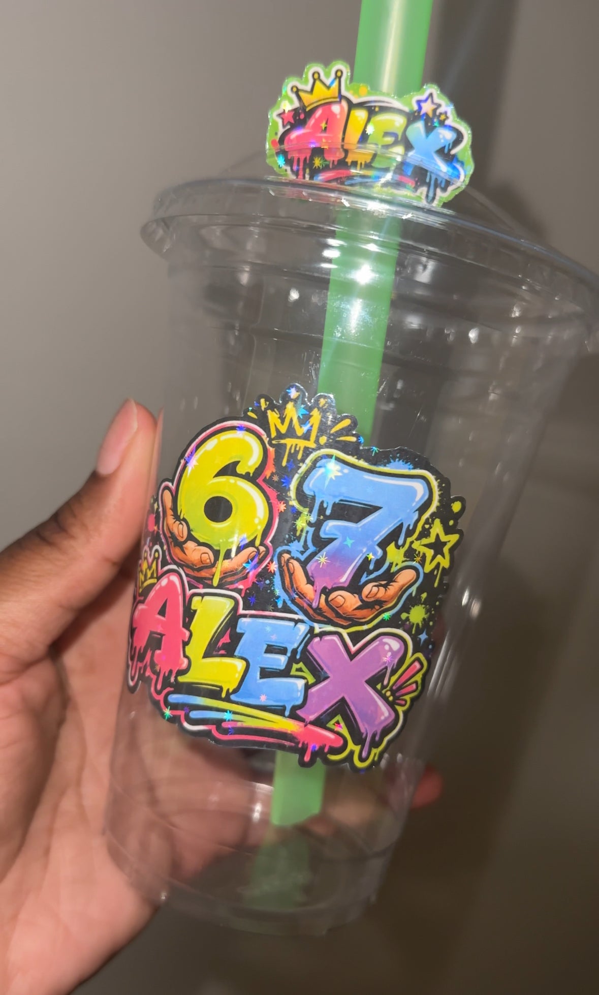 Customized 6 7 birthday Clear plastic cup with colorful text and a straw, held by a hand.