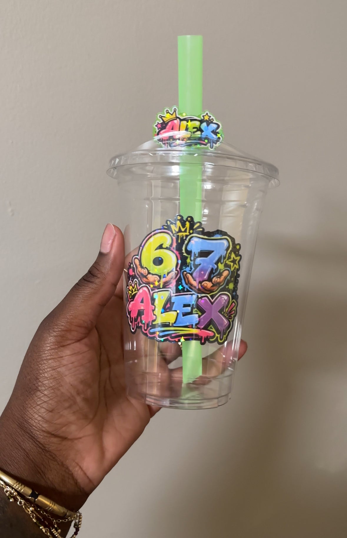 Customized birthday Clear plastic cup with colorful design and straw held by a hand against a neutral background
