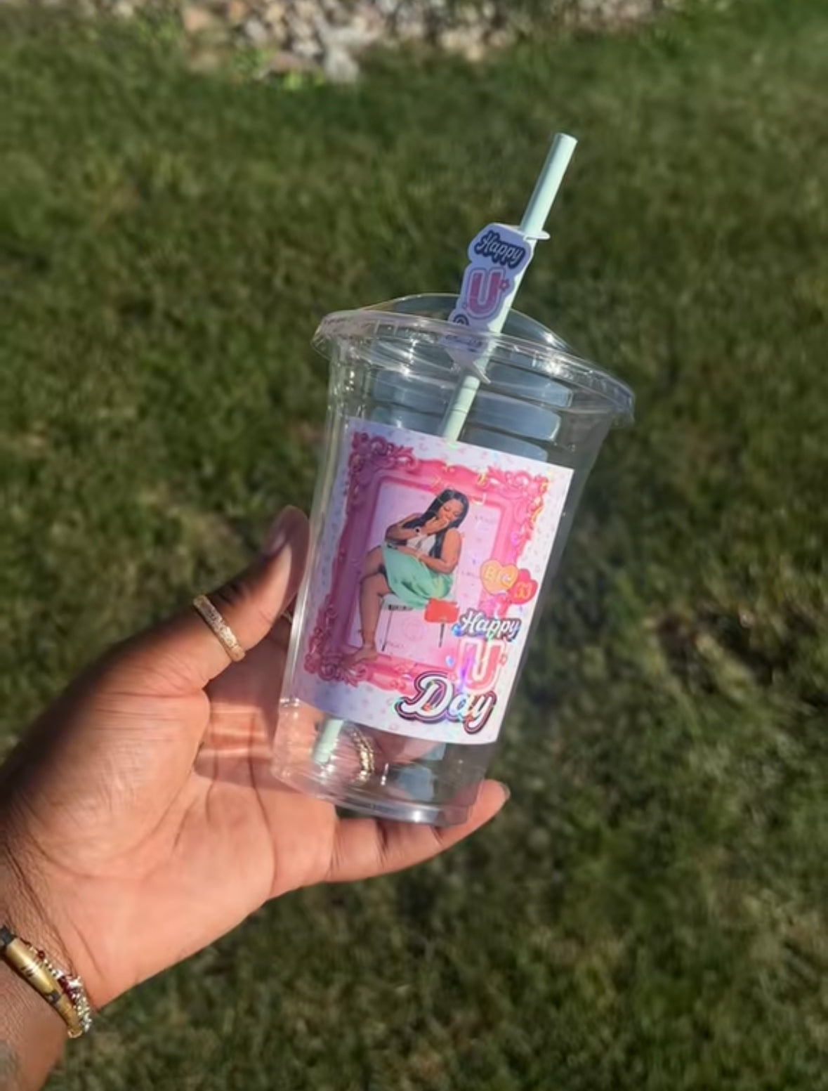 Custom birthday Clear plastic cup with a colorful label held by a hand against a grassy background